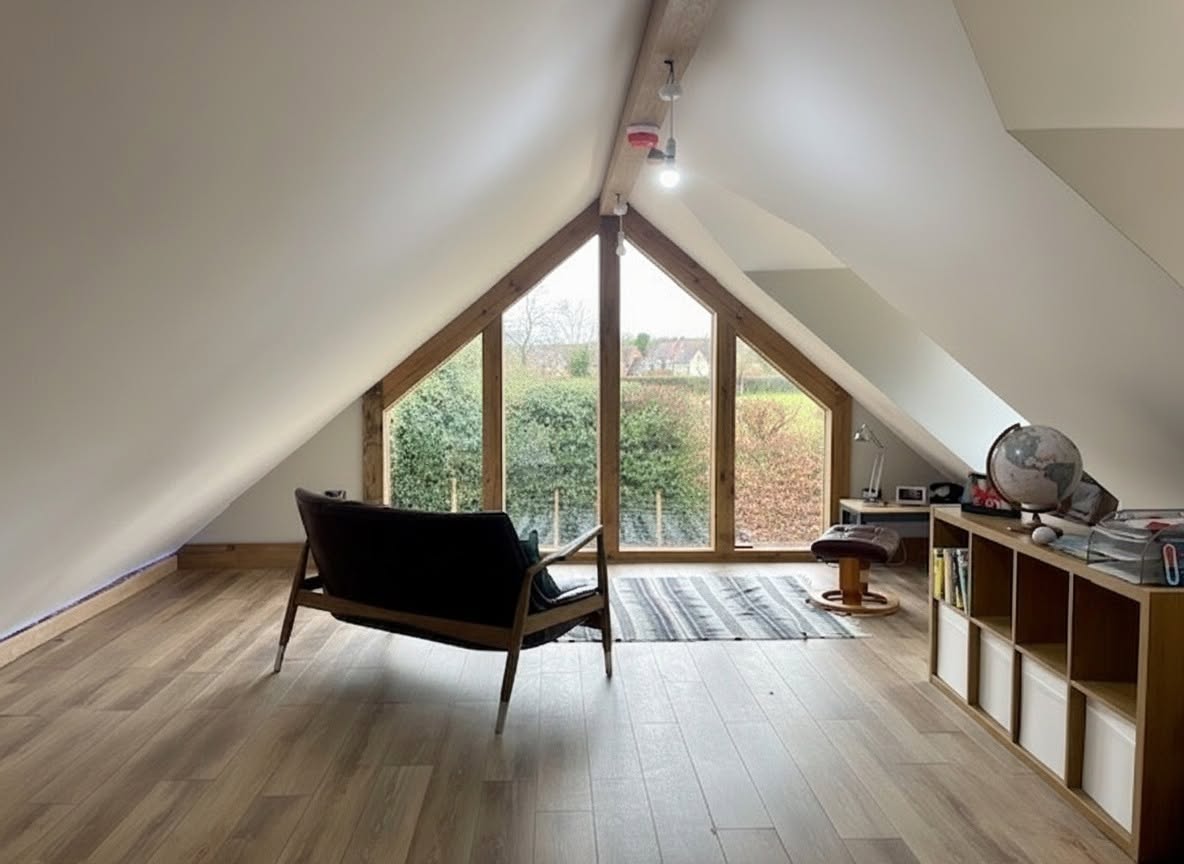 Loft conversion bedroom with a large triangular gable window and countryside view