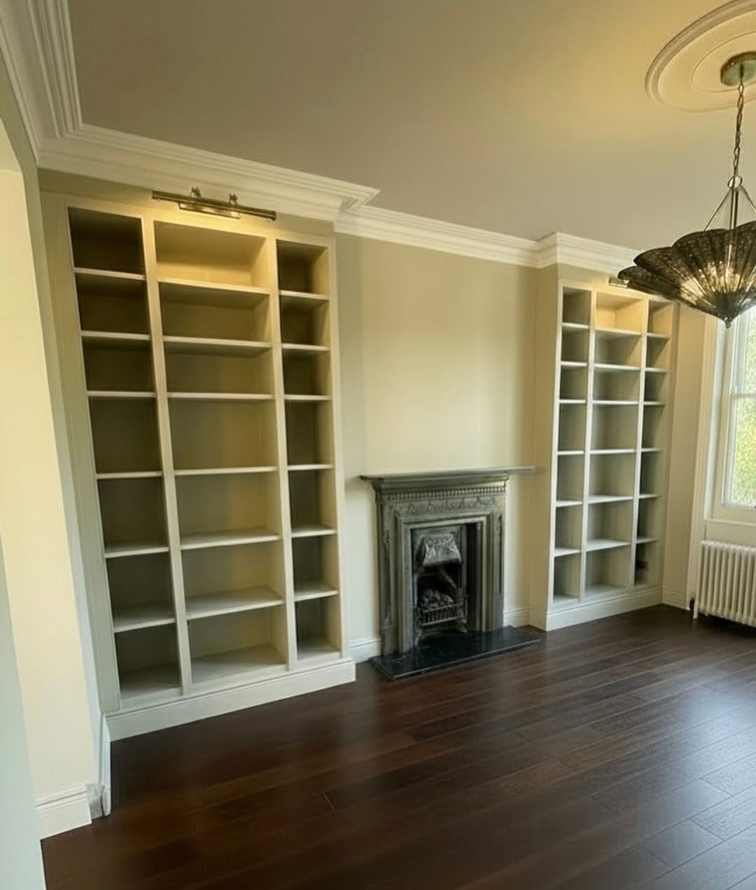 Refurbished reception room with fitted olive-green bookcases and a decorative fireplace