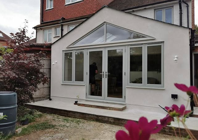 Dining area lit by triangular gable glazing and grey-framed glass doors in a home extension
