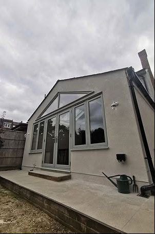 Exterior of a rendered rear extension with grey-framed glazing and a gable window