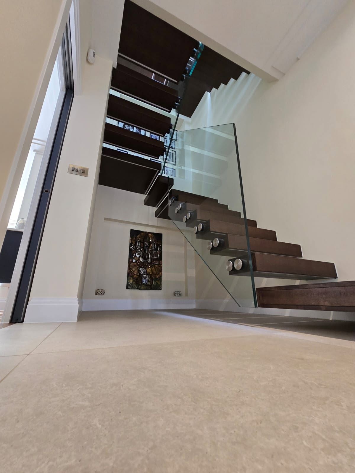 Floating timber staircase with structural glass balustrade beside full-height glazing