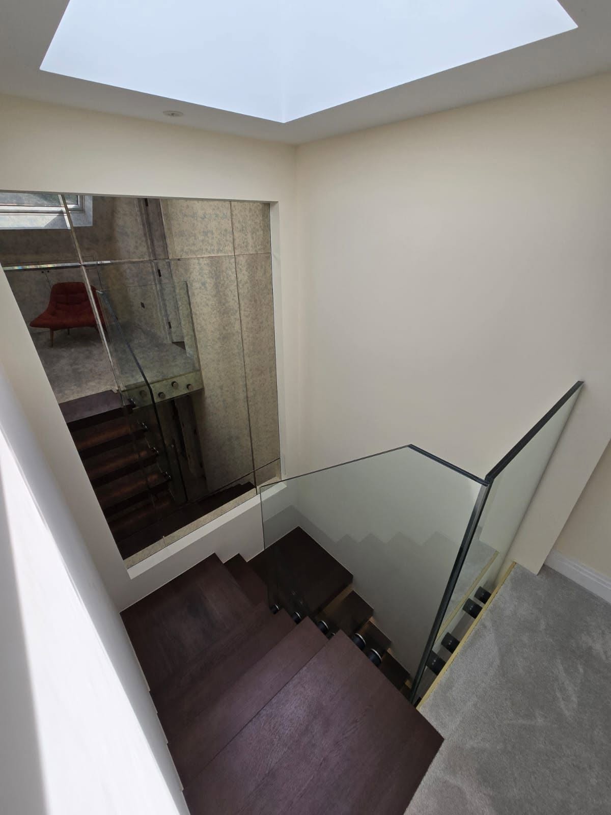 Stairwell viewed from above showing glass balustrade panels and plastered white walls
