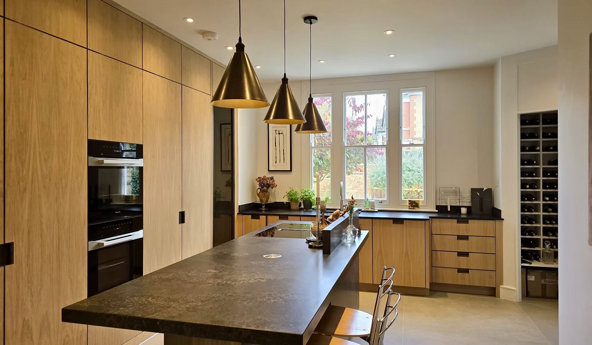 Kitchen with full-height oak cabinetry, dark stone island and brass pendant lighting
