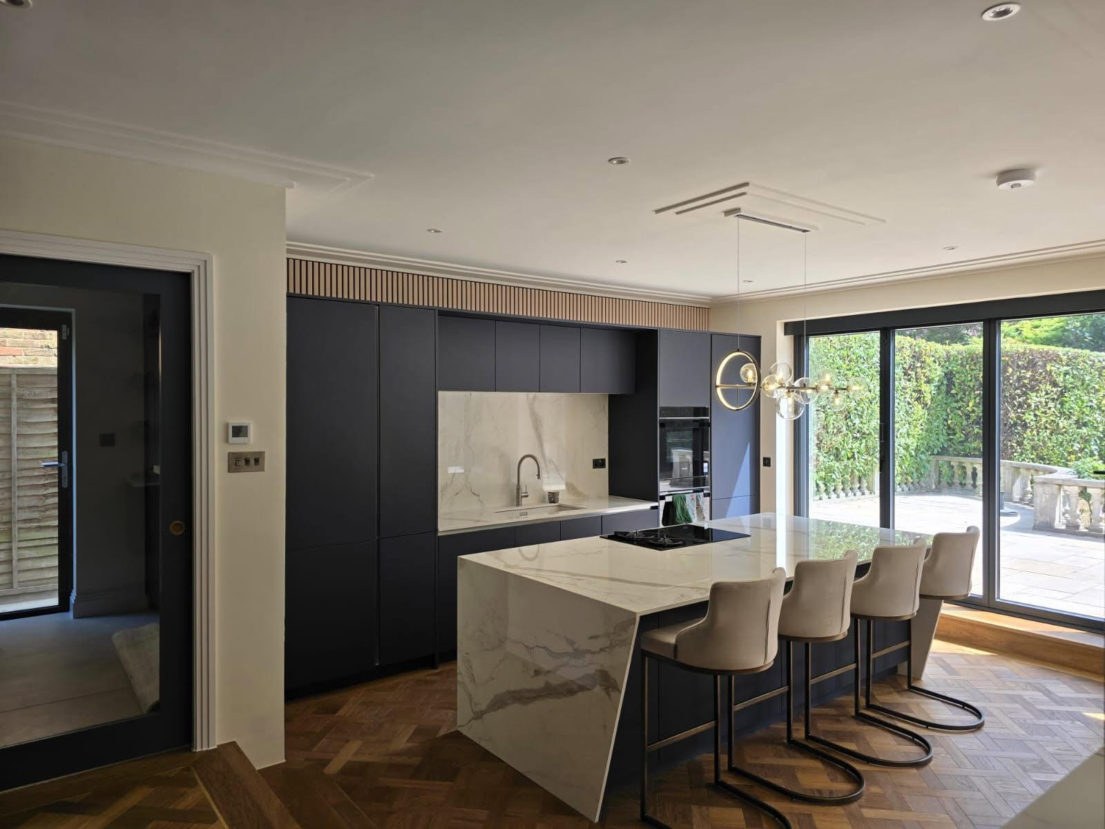 Kitchen extension with matt navy cabinetry, marble waterfall island and sliding glass doors