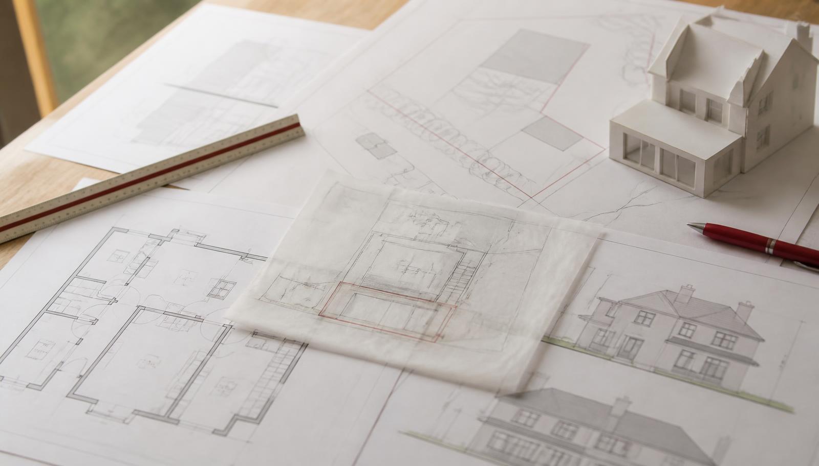 Planning application site plans, elevations and a tracing paper overlay laid out on a desk